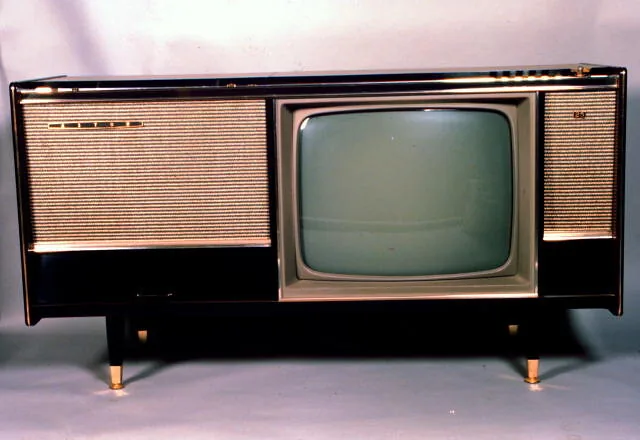 A long, low wooden console on splayed legs, a small television screen in the middle between two fabric speaker panels.